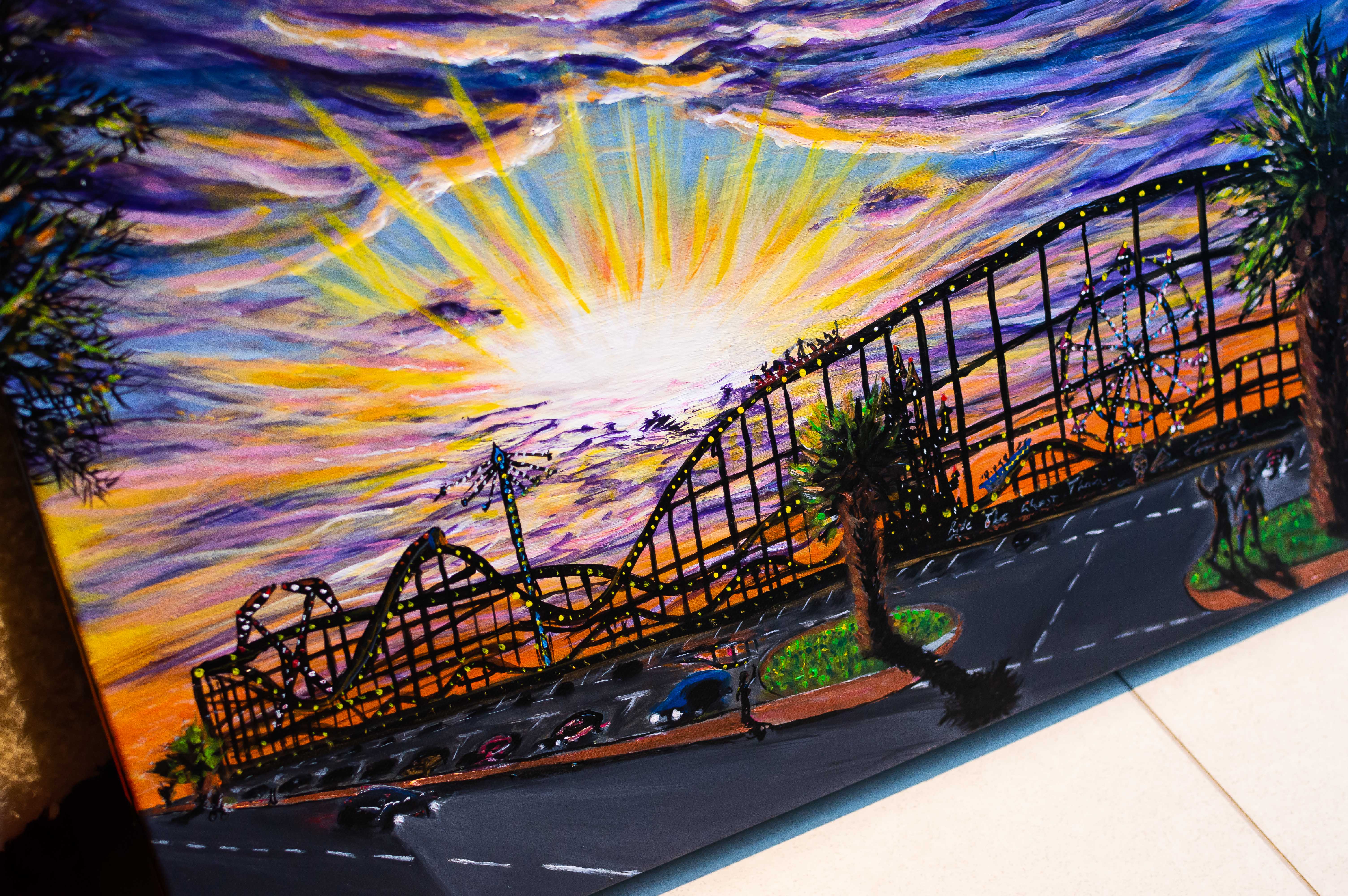 A colourful scene portraying an amusement park at dusk, with blues/yellows/oranges/purples across a starry sky and dramatic clouds. Figures are seen in the foreground watching the rollercoaster, and a car is headed in the direction of the viewer.